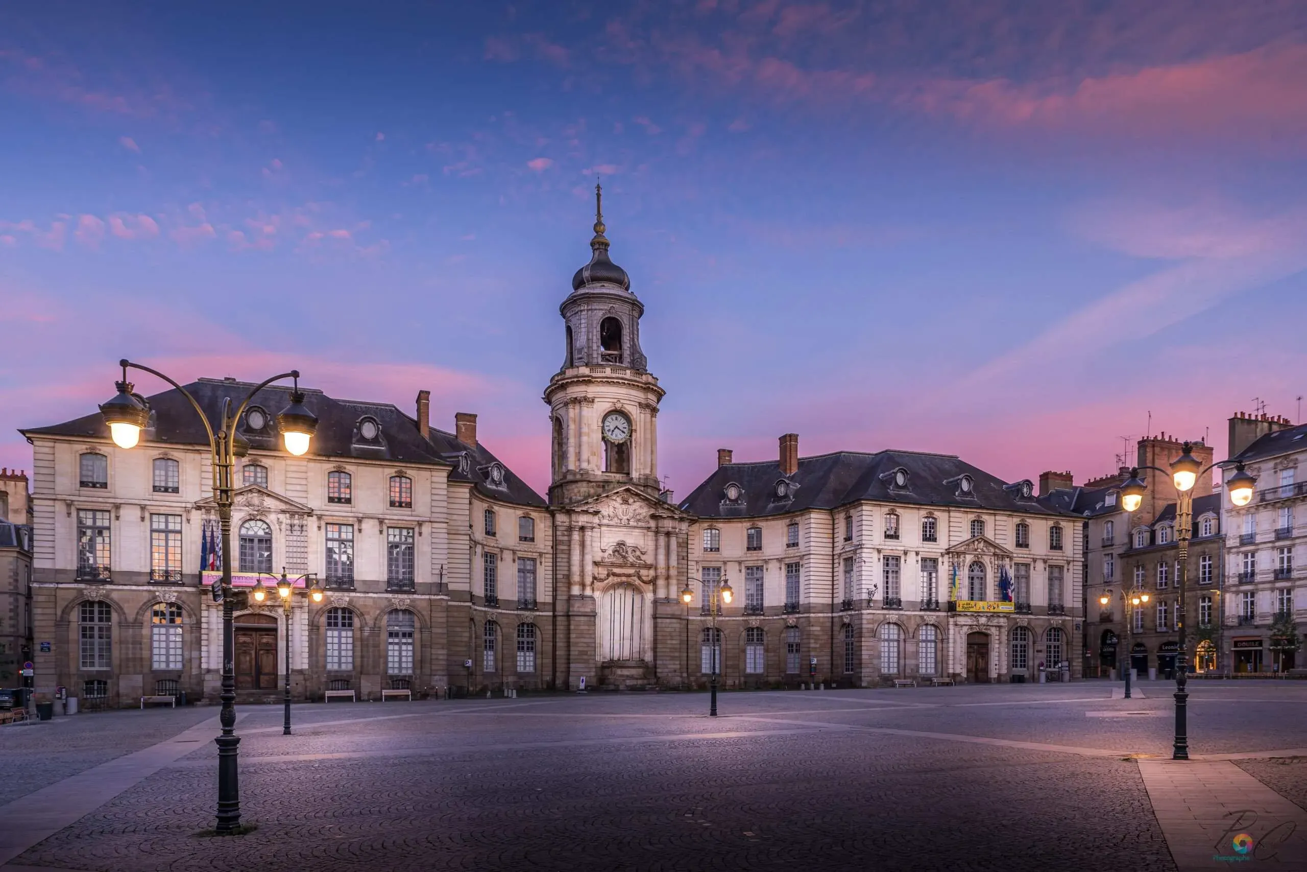 Place de la Mairie de Rennes illuminée au crépuscule sous un ciel rose.