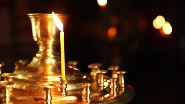Une fine bougie jaune allumée sur un grand chandelier doré dans une église sombre.